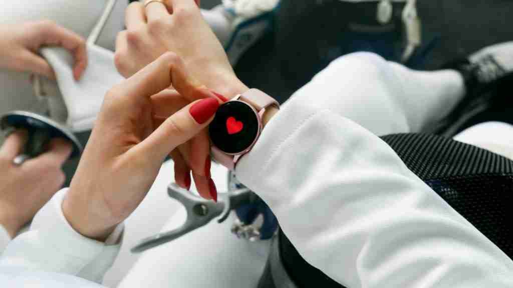 Elegir tu reloj inteligente oro rosa encendido con un corazón rojo en el medio, siendo manipulado por una persona.